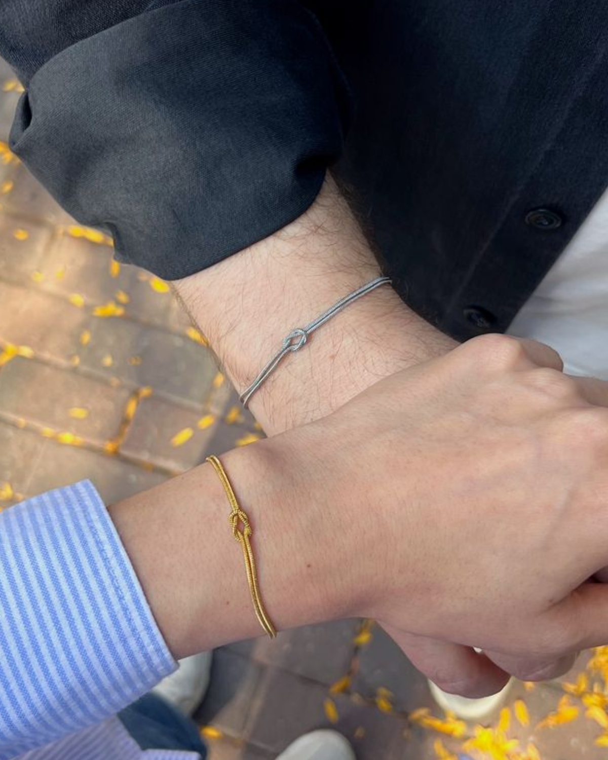 Couple holding hands wearing silver and gold knot bracelets