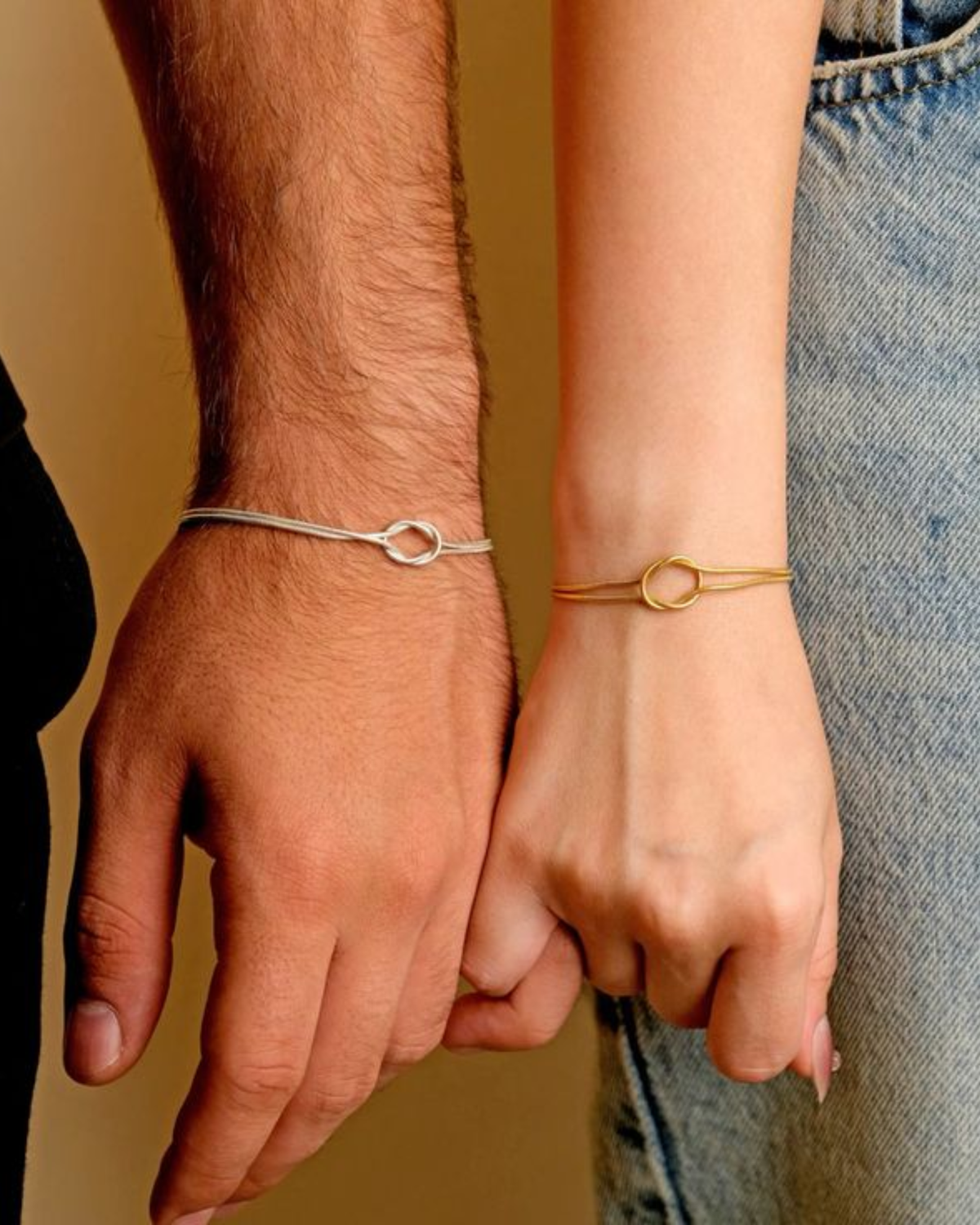 Couple wearing matching love knot promise bracelets, silver on him and gold on her