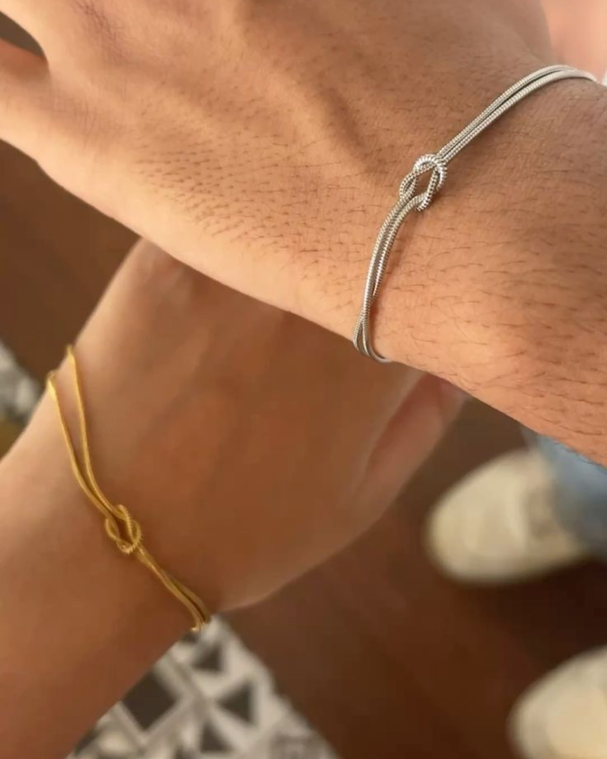 Silver and gold love knot bracelets worn by a couple